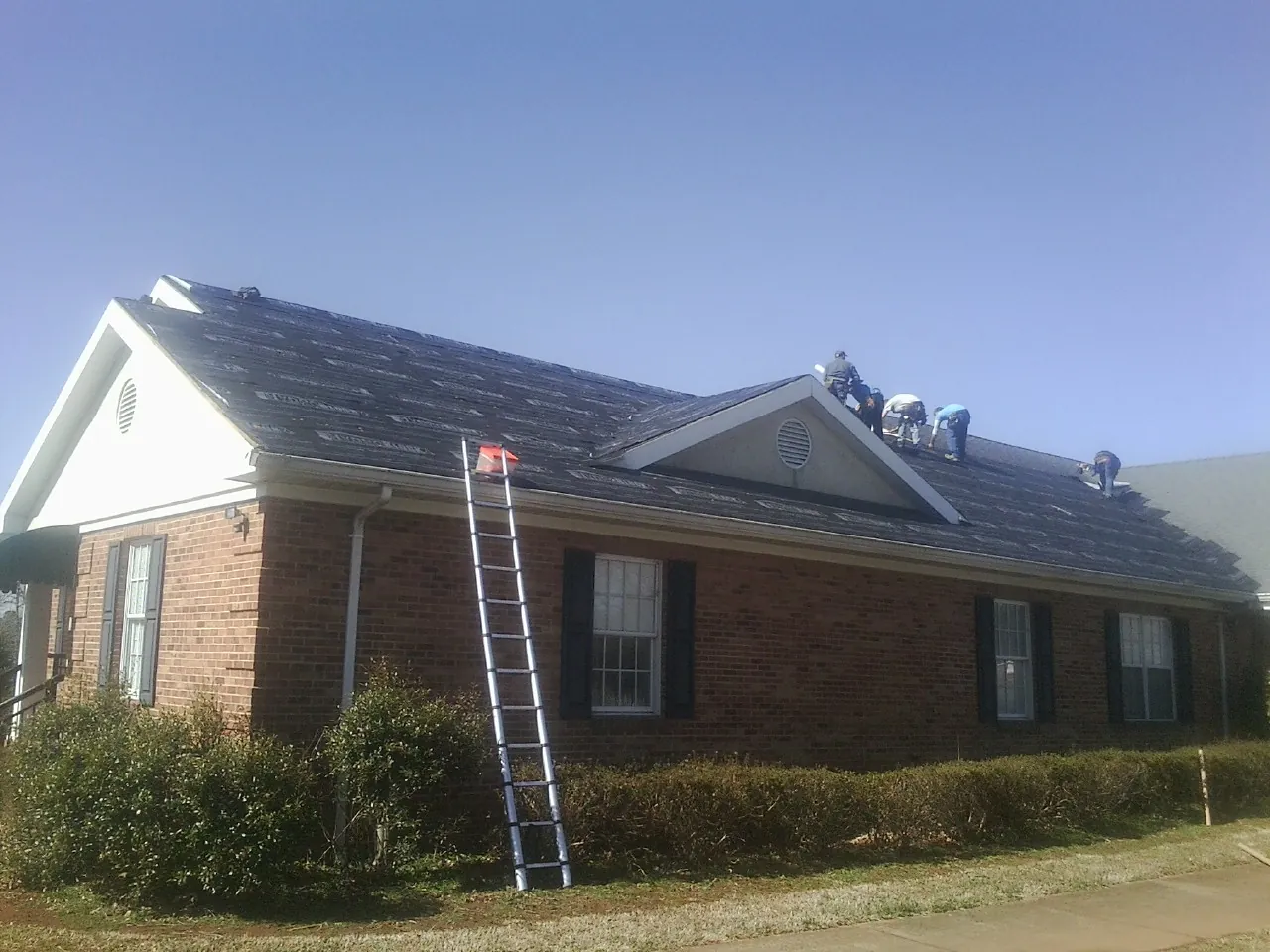 Crew tearing shingles off a brick ranch roof with a ladder set — Metal Roof Repair work by our crew in Clearlake