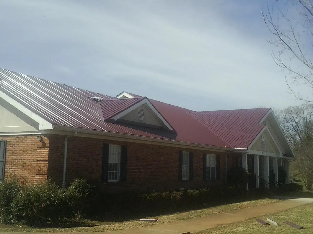 Red metal roof with gabled entries on a long brick building, from a Hail Damage Roof Repair job in Clearlake