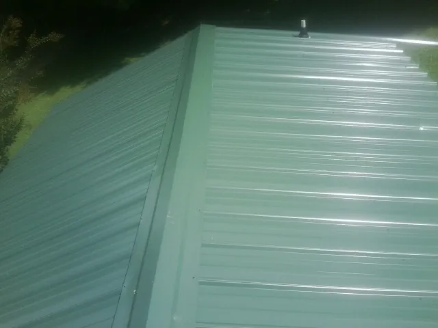 New green metal panels meeting at the ridge of a roof — Flat Roof Repair work by our crew in Clearlake